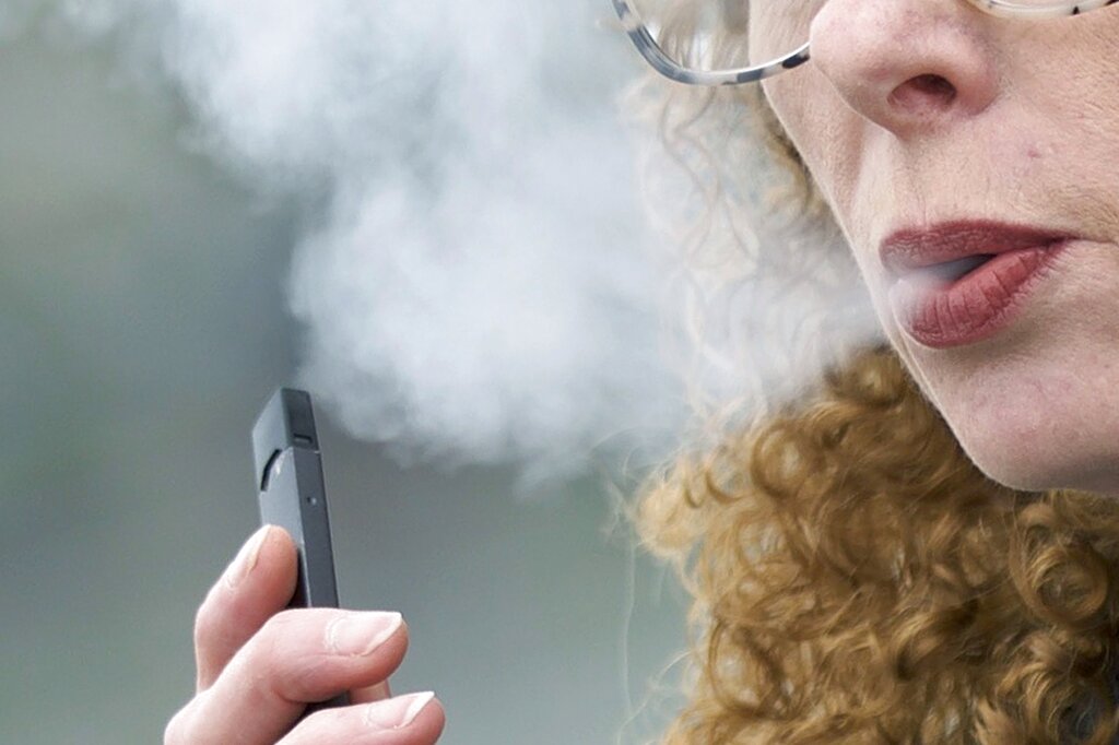 In this April 16, 2019 file photo, a woman exhales while vaping from a Juul pen e-cigarette in Vancouver, Washington.
