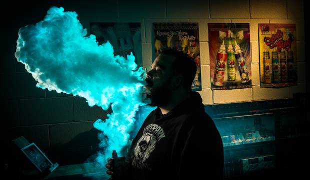 Backlit profile of man exhaling blue smoke cloud